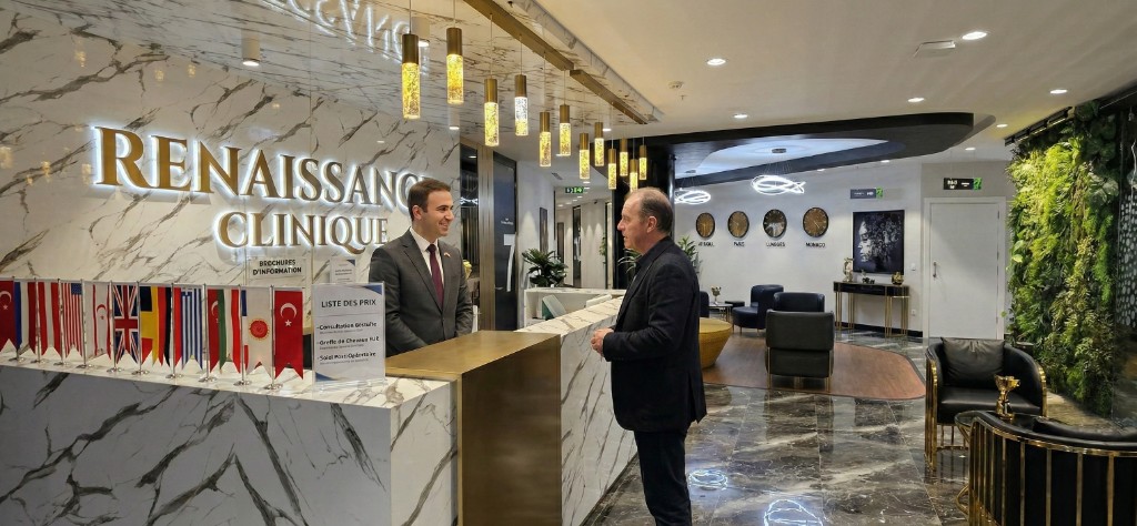 Réception et salle d'accueil de Renaissance Clinique à Istanbul : intérieur luxueux avec sol en marbre, éclairage chaleureux, mur végétal et drapeaux internationaux. Un coordinateur francophone en costume accueille un patient à la réception, avec les horloges des villes francophones (Paris, Londres, Monaco) et l'enseigne Renaissance Clinique en arrière-plan