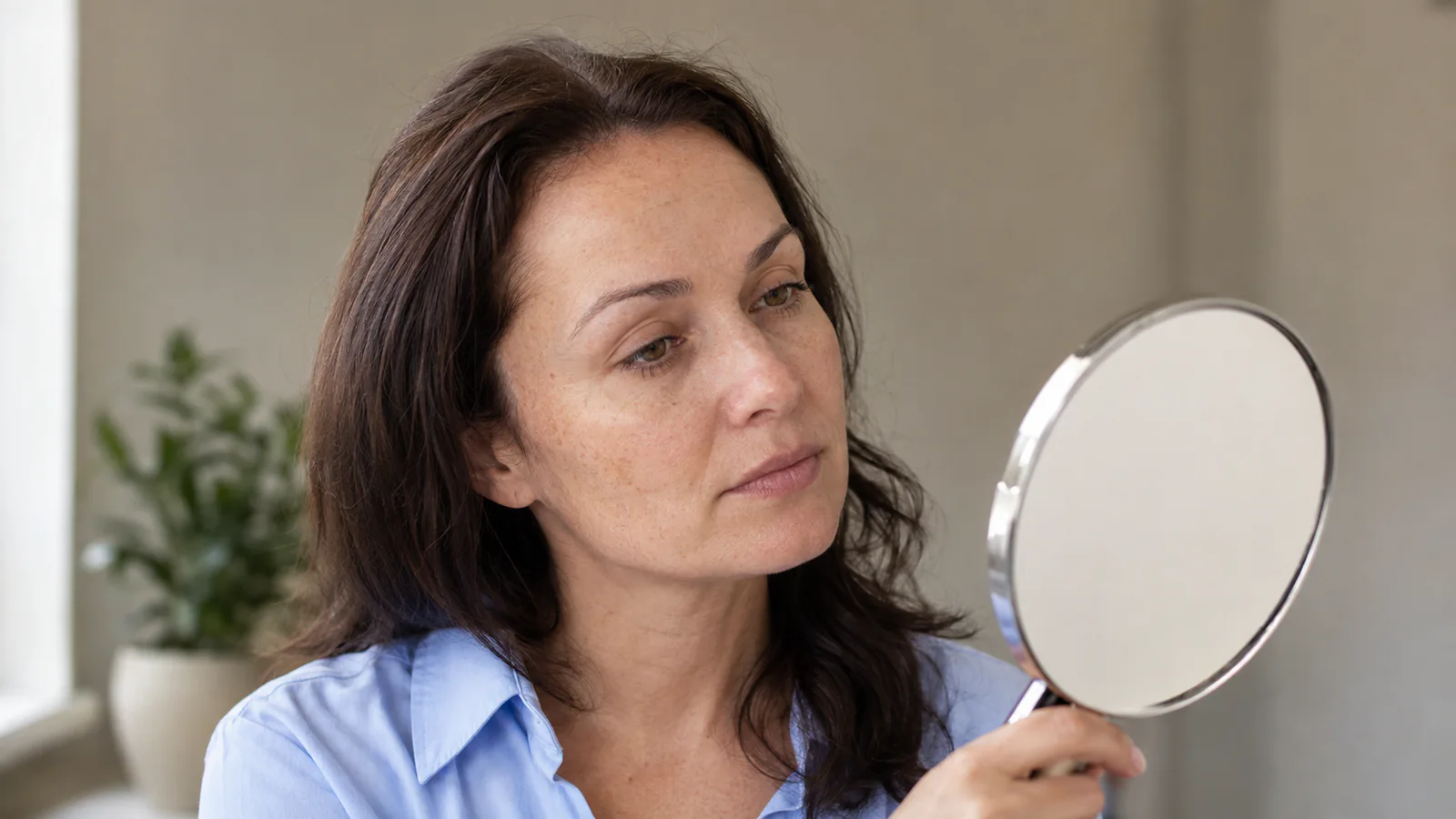 Une femme observe ses sourcils naturellement clairsemés dans un miroir de consultation.